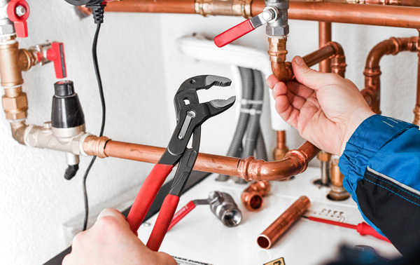 person using pliers to tighten copper pipes in plumbing system focusing on maintenance tools for home repairs related to 13 plumbing tips